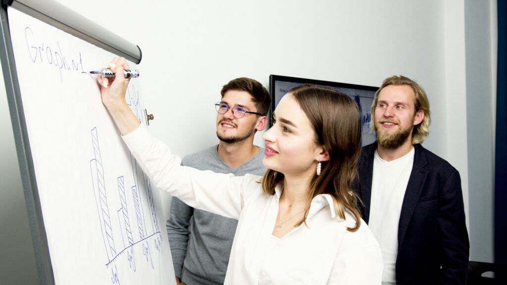 Drei Menschen im Business-Look erarbeiten an einem Whiteboard einen Graphen.